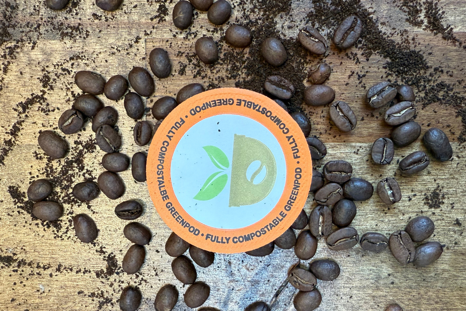  compostable coffee pod surrounded by coffee beans on a wooden surface