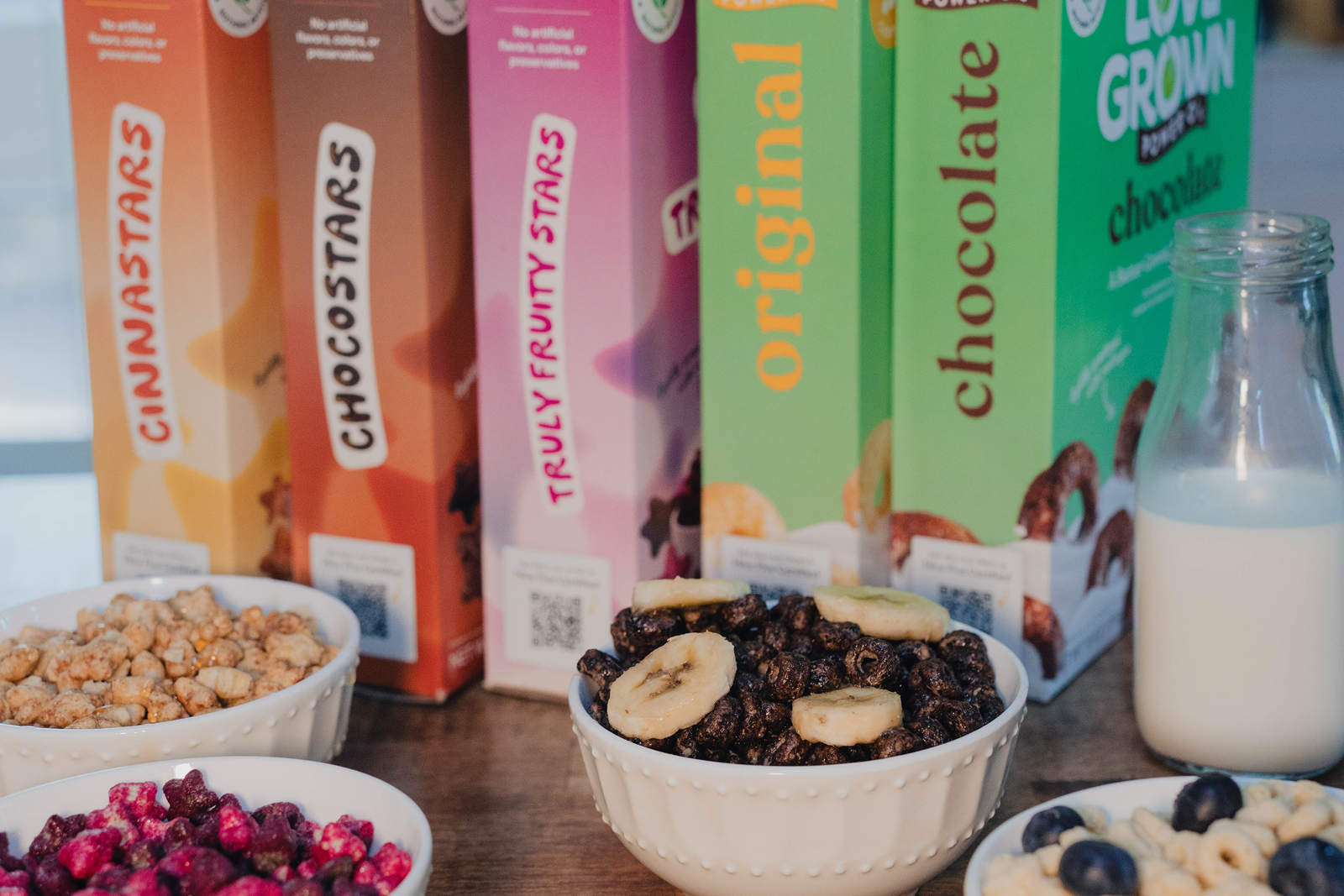 Assorted Love Grown food packaging with bowls of snacks on a wooden surface.