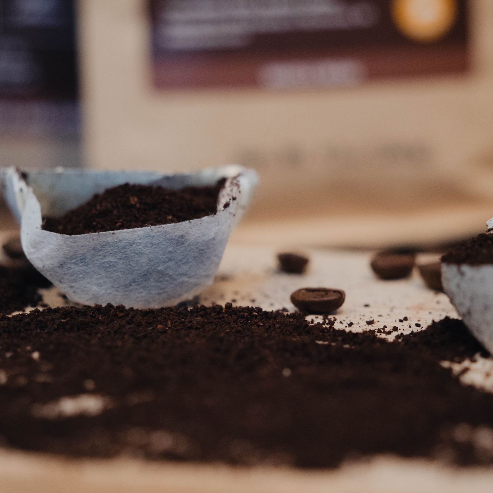 Close-up of coffee grounds and a filter on a wooden surface with a blurred background.
