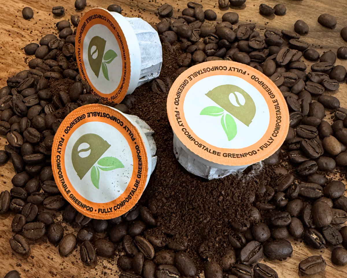 Three compostable coffee pods on a wooden surface with coffee beans around them.