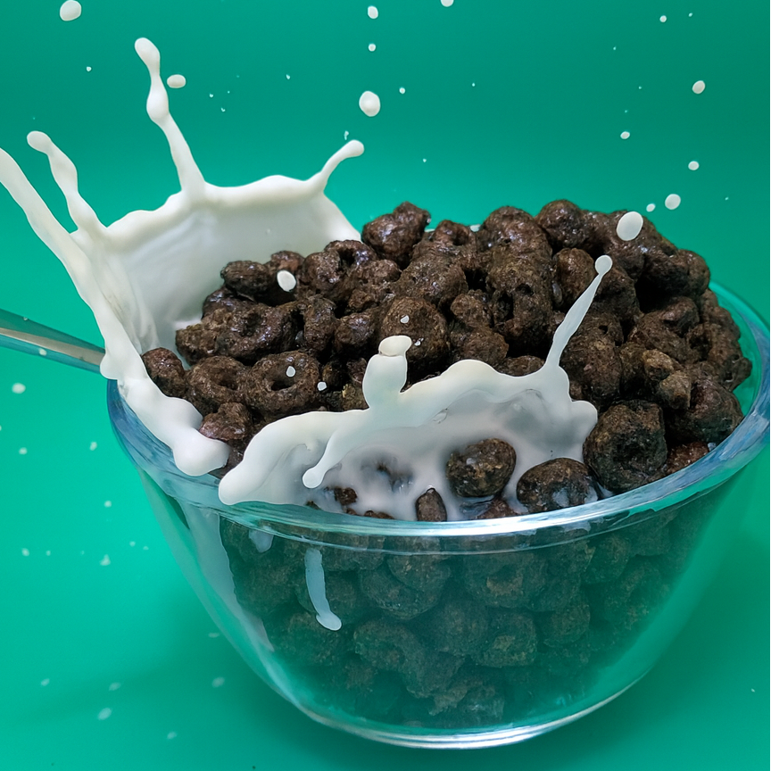 Chocolate cereal being poured into a bowl with milk against a green background