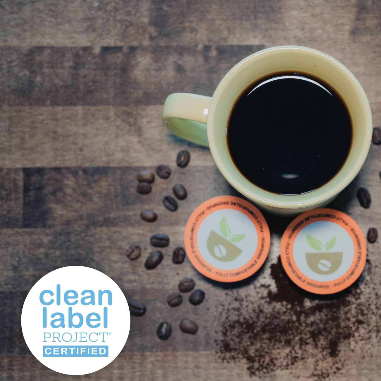 Green mug with coffee and coffee beans on a wooden surface, featuring Clean Label Project certification logo.